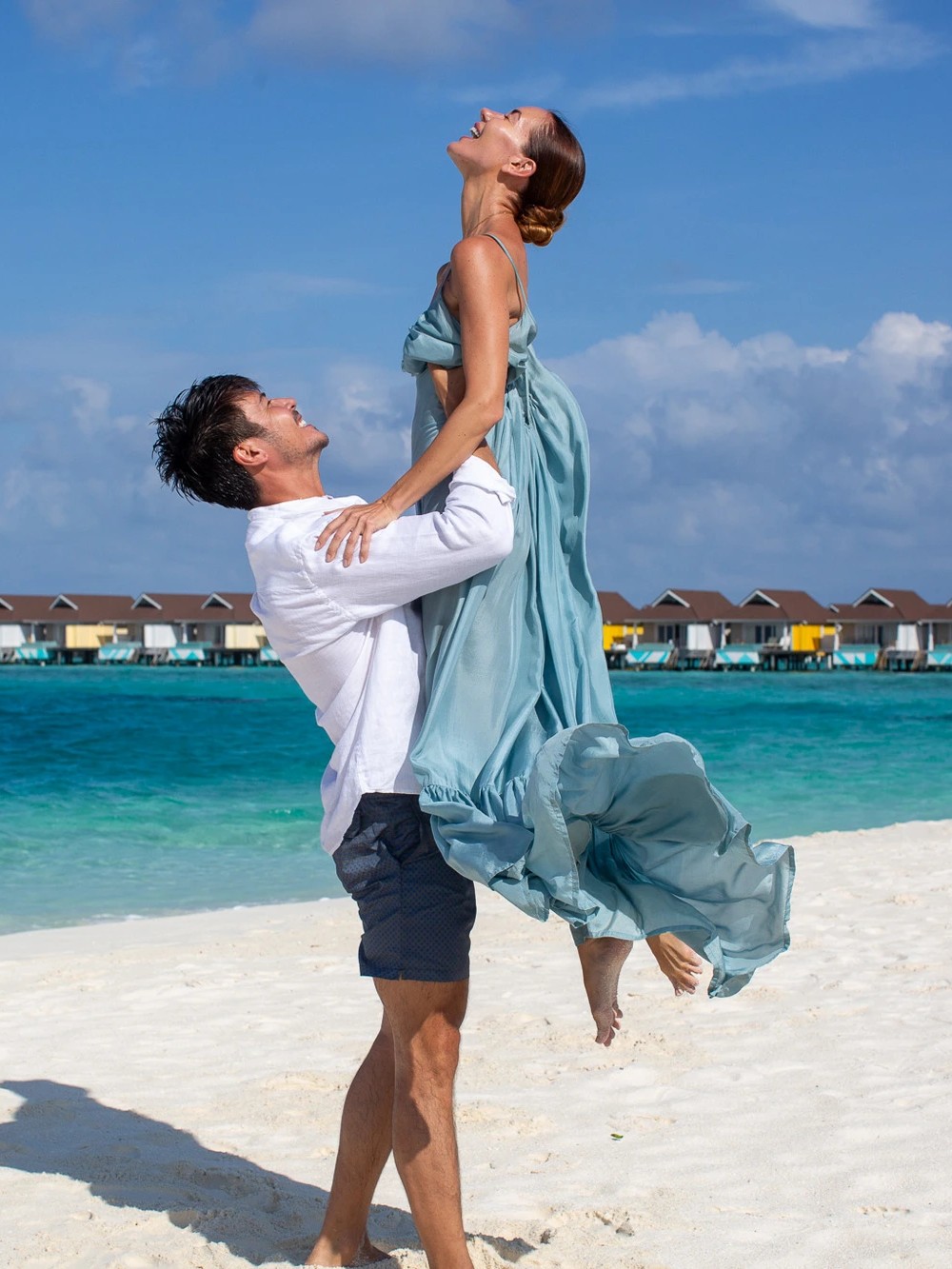 Joyful couple on a white-sand beach in front of overwater villas